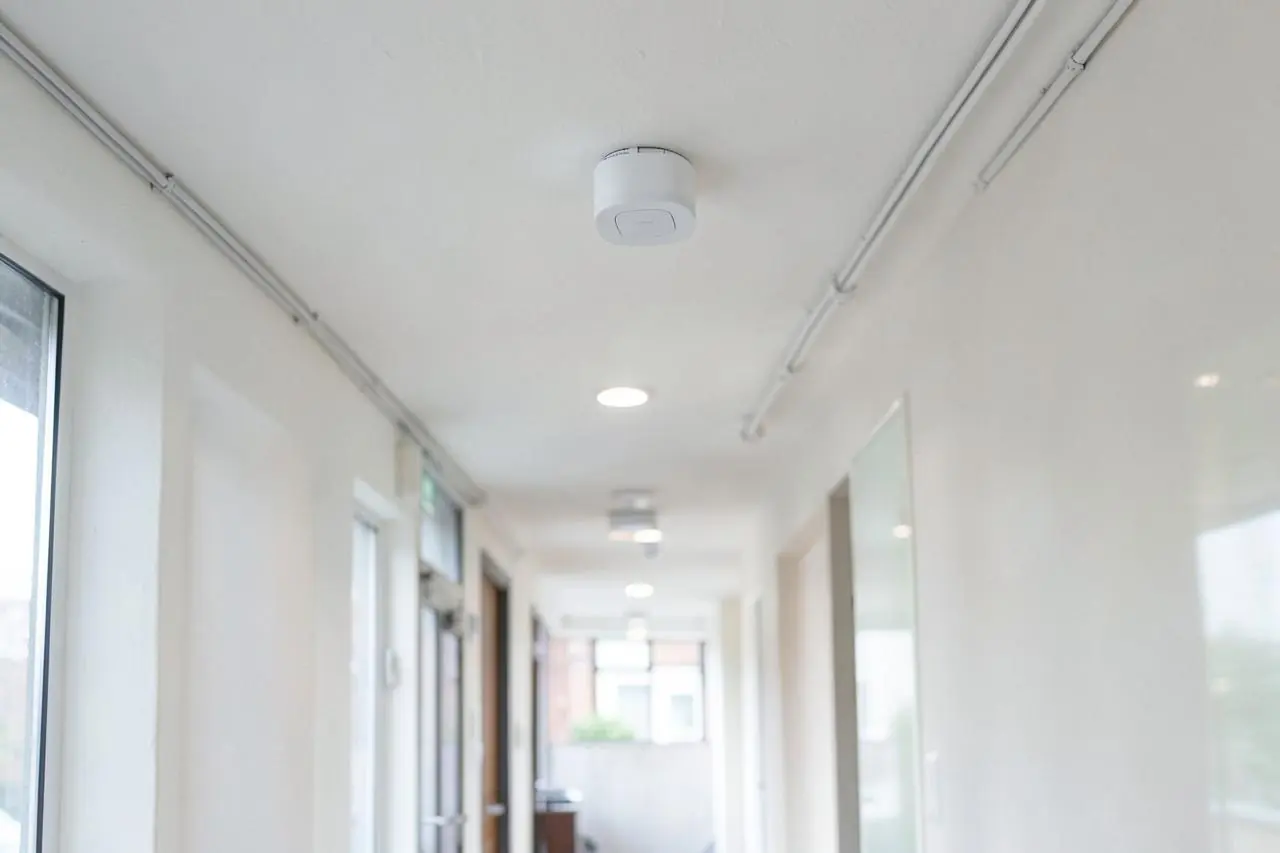 Discreet white ceiling-mounted wireless access point in a London commercial hallway
